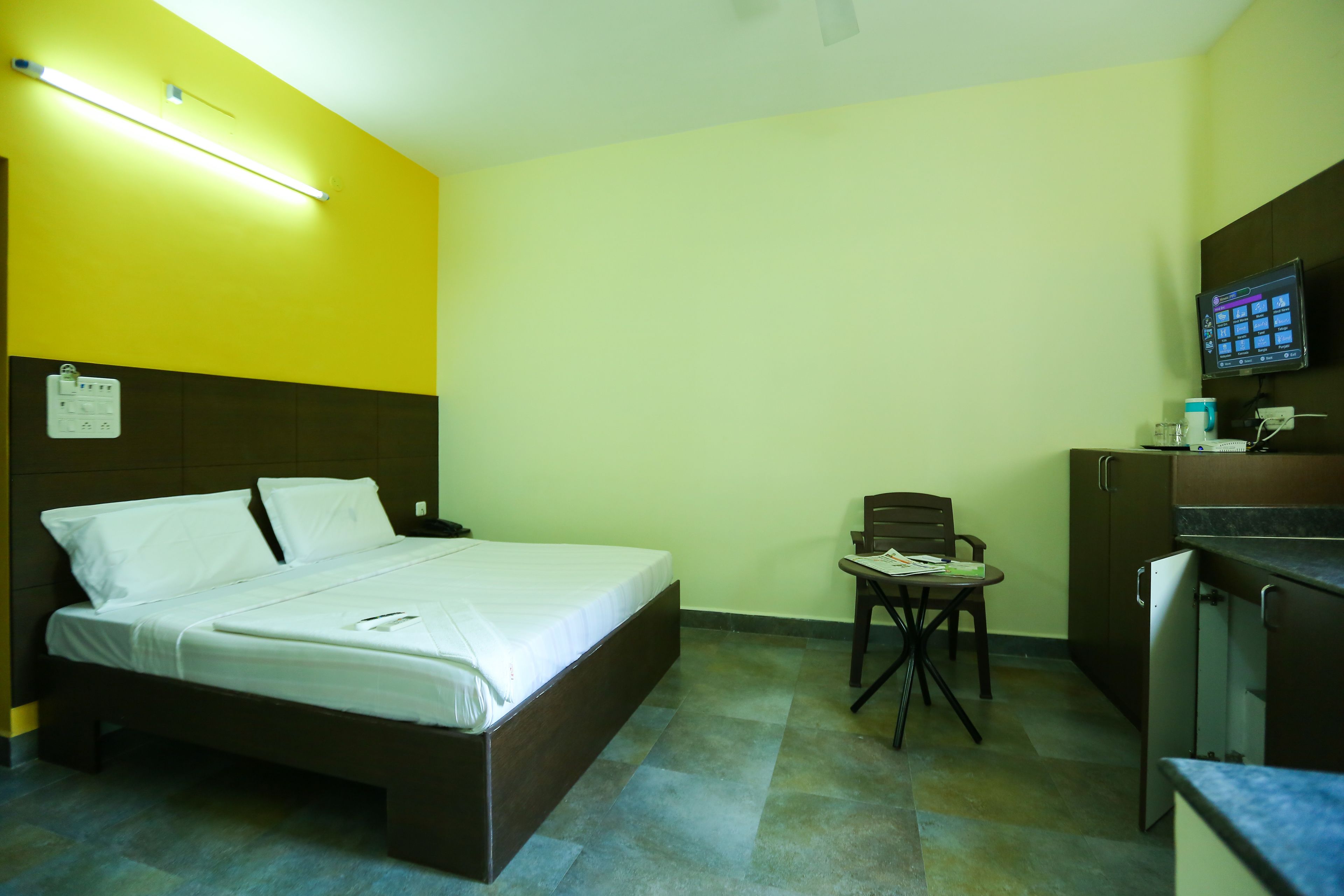 A hotel room with a bed, a desk, a chair, a television, and a small kitchenette.