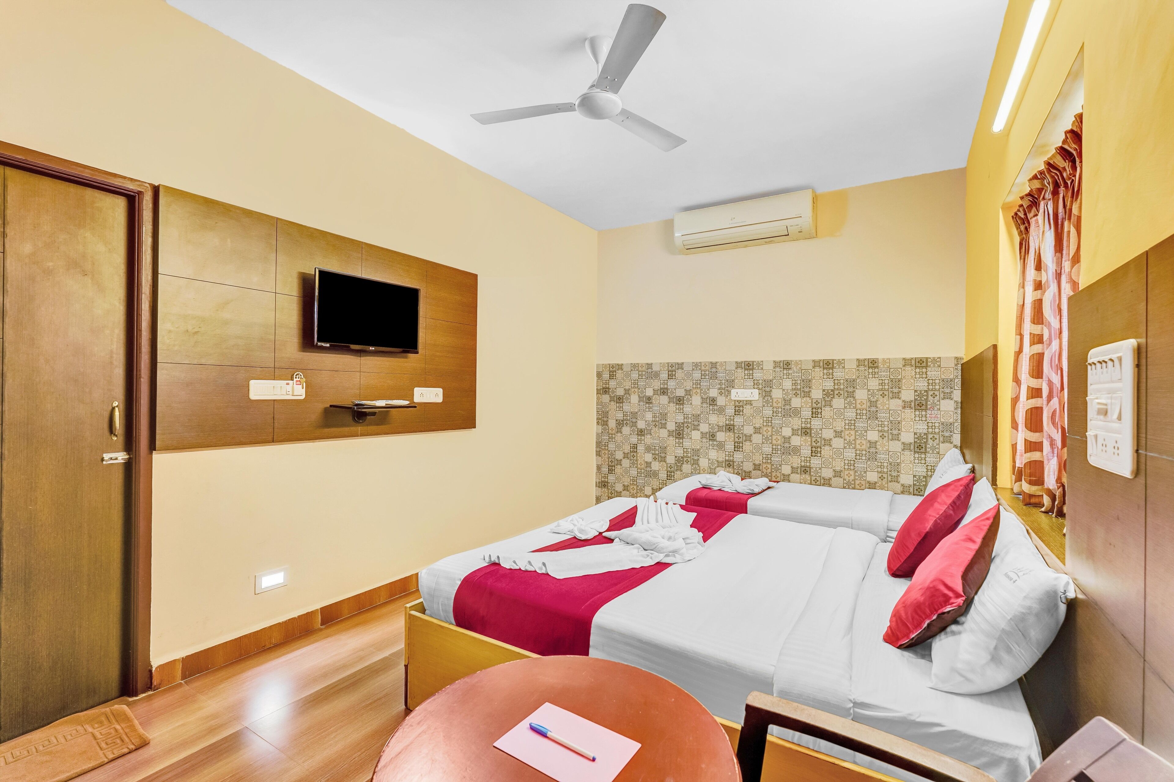 A hotel room with two beds, a television, a ceiling fan, and an air conditioning unit.