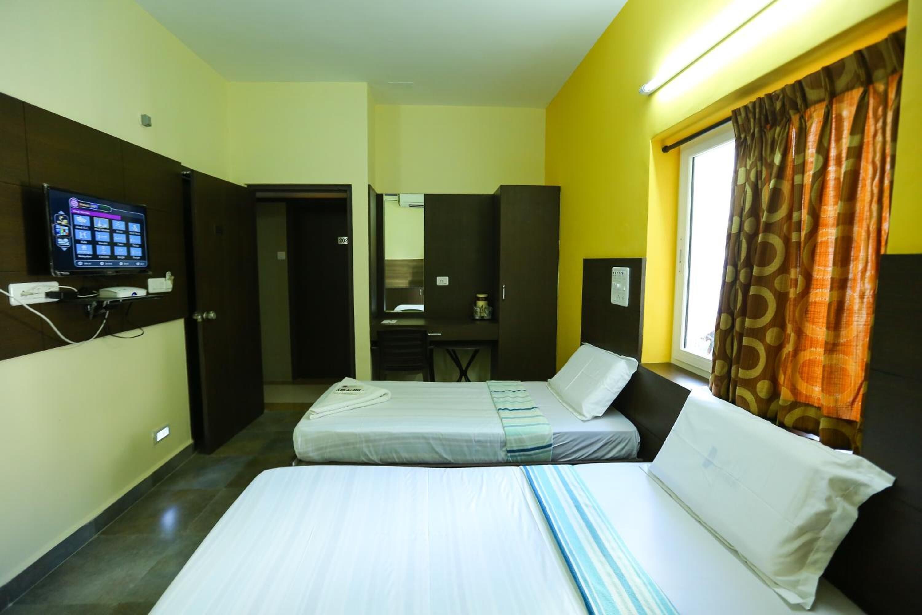 Ein Hotelzimmer mit zwei Betten, einem Fernseher, einem Schreibtisch und einem durchgegangenen Tür erkennbaren Badezimmer.