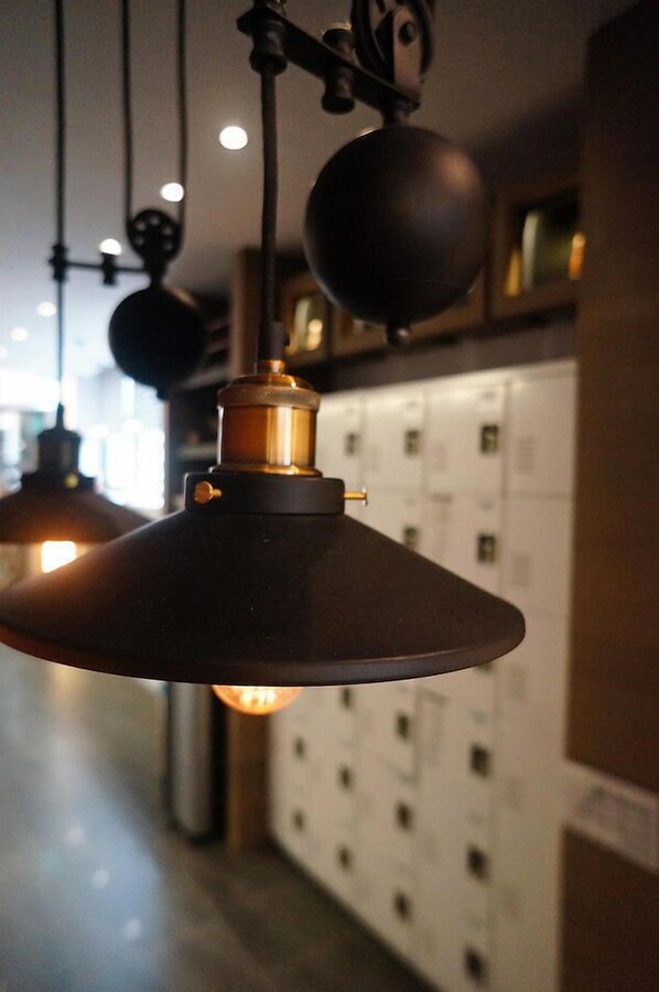Luminária pendente com cúpula cônica e detalhe em latão, pendurada em um corredor com armários ao fundo.
