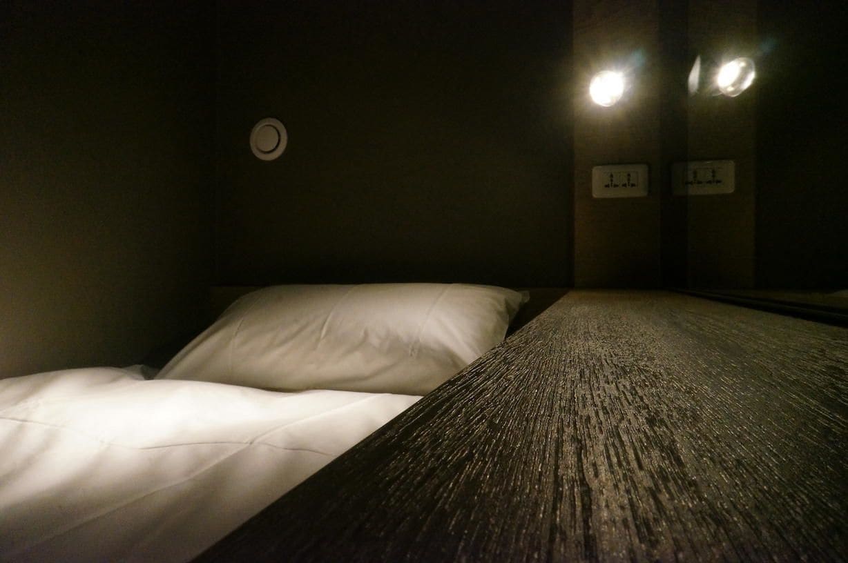 Una cama individual con ropa de cama blanca en una habitación con poca luz.