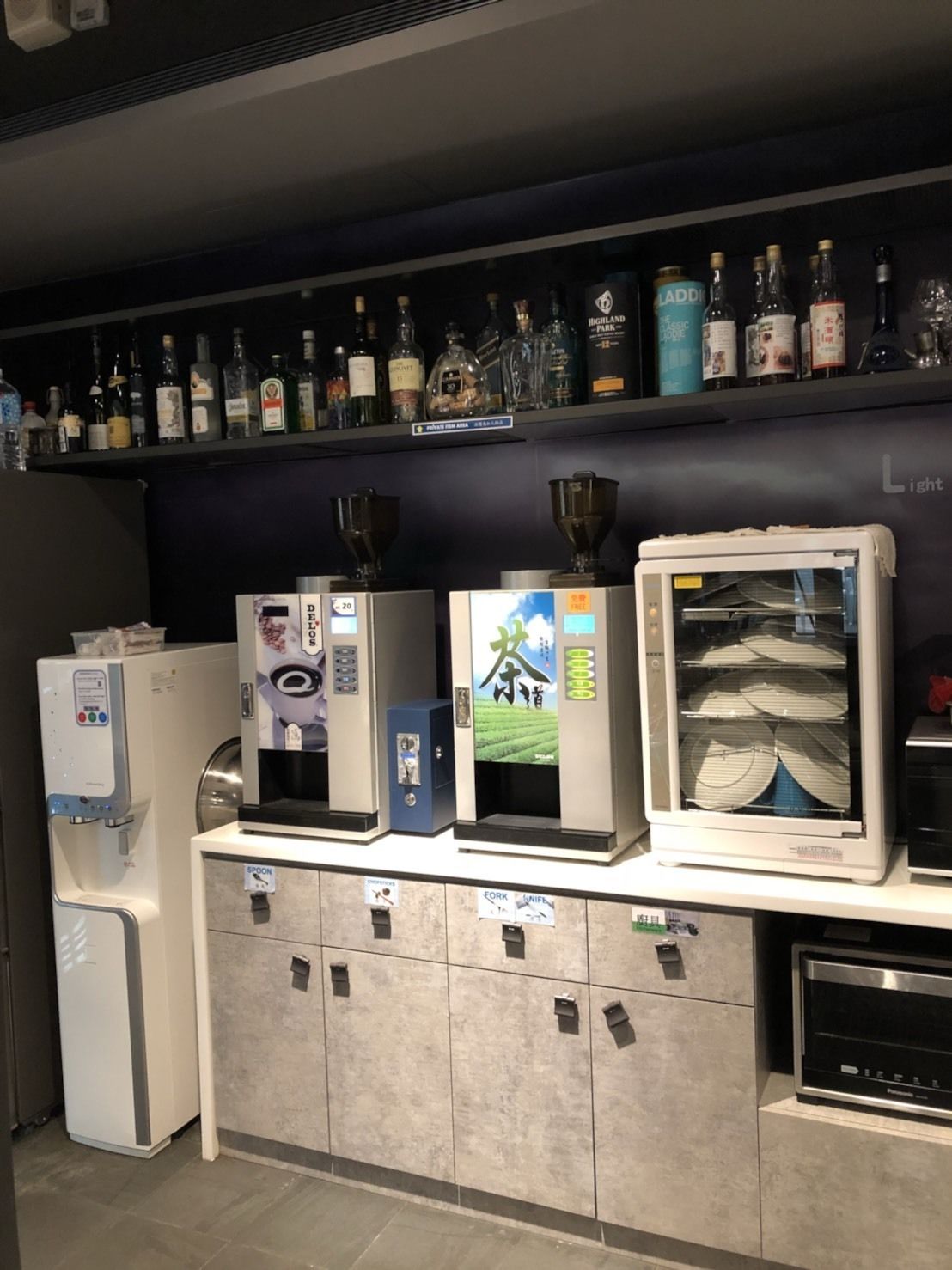 A kitchen area with a coffee machine, a refrigerator, a microwave, and a shelf with various bottles.