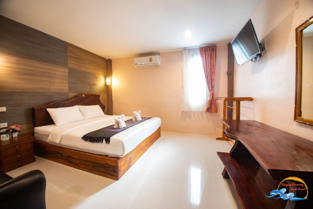 Una habitación de hotel moderna con una cama de madera, un televisor de pantalla plana y un escritorio de madera.