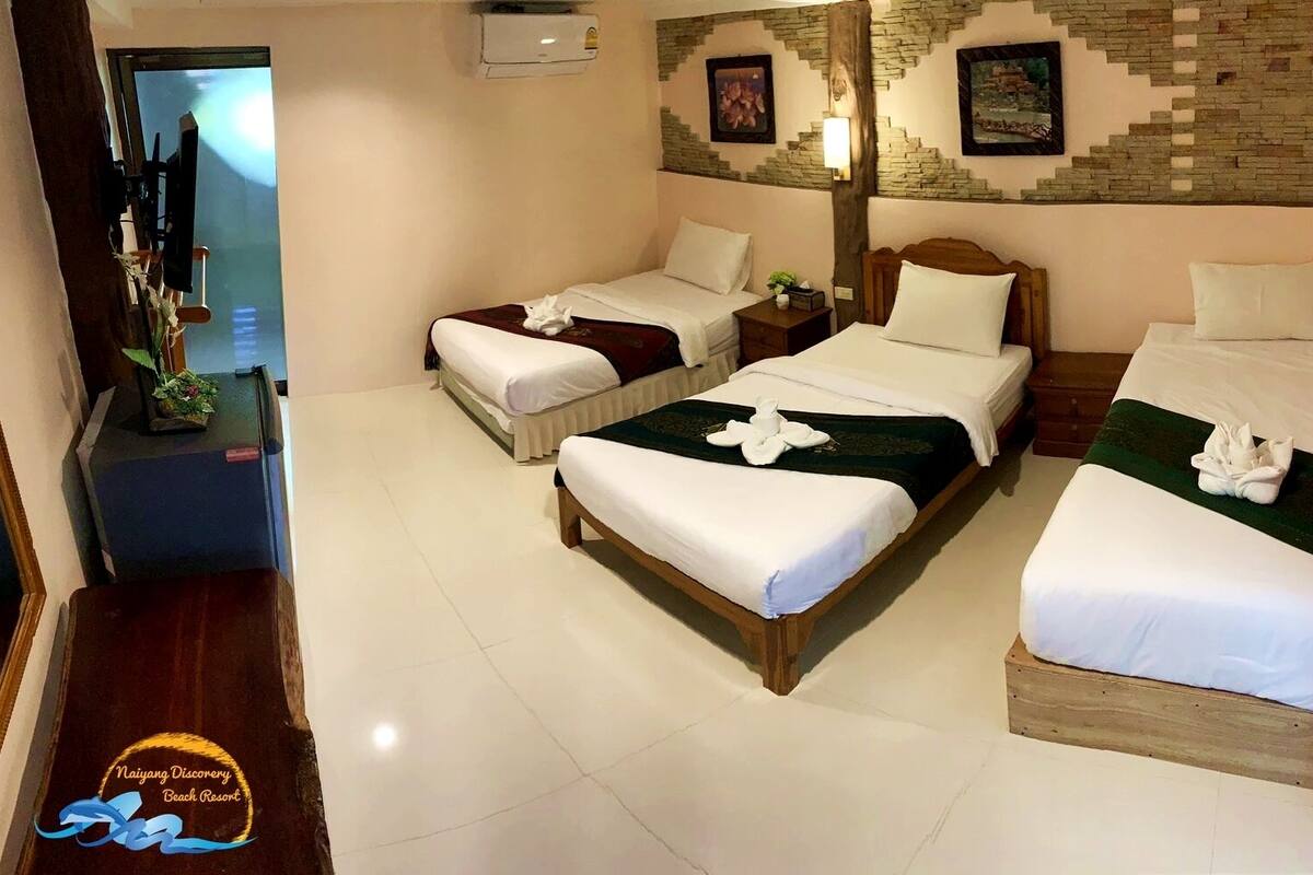 Habitación de hotel con tres camas, cabecera de madera, piso de baldosas y pared con diseño de piedra.