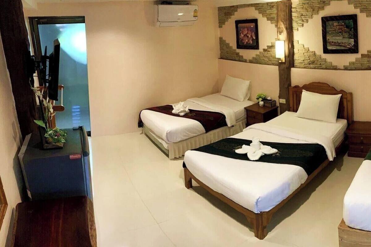 Habitación de hotel con tres camas, un televisor, una mesita con una planta y una pared con diseño de ladrillo.