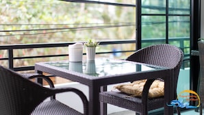 Un balcón con mobiliario de mimbre, una mesa de vidrio y una planta en maceta.