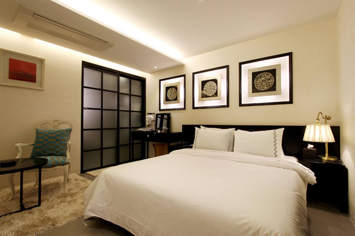 A hotel room with a large bed, a chair, a nightstand, and framed artwork on the wall.