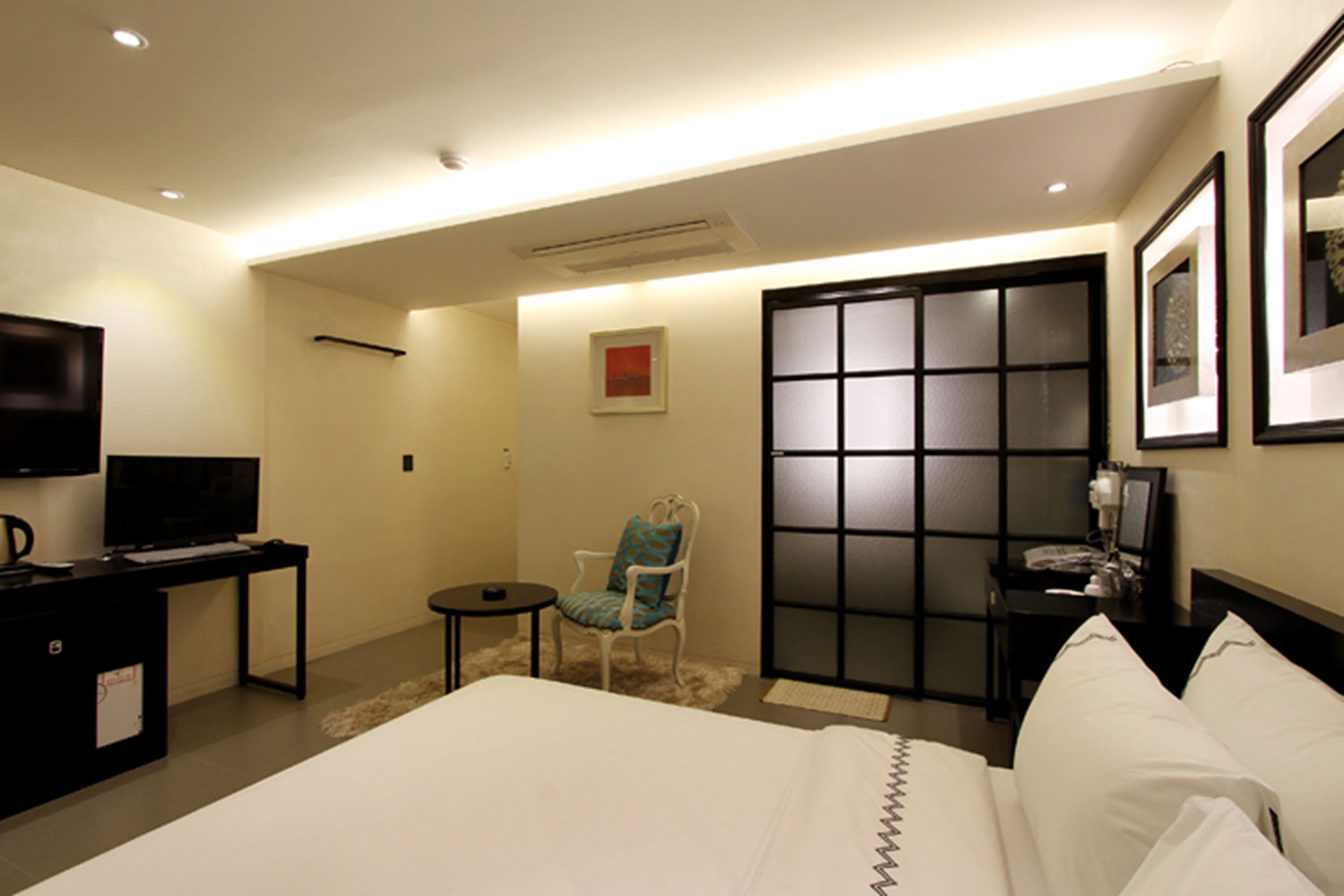 Habitación de hotel con cama, televisor, escritorio, silla y puerta corrediza.