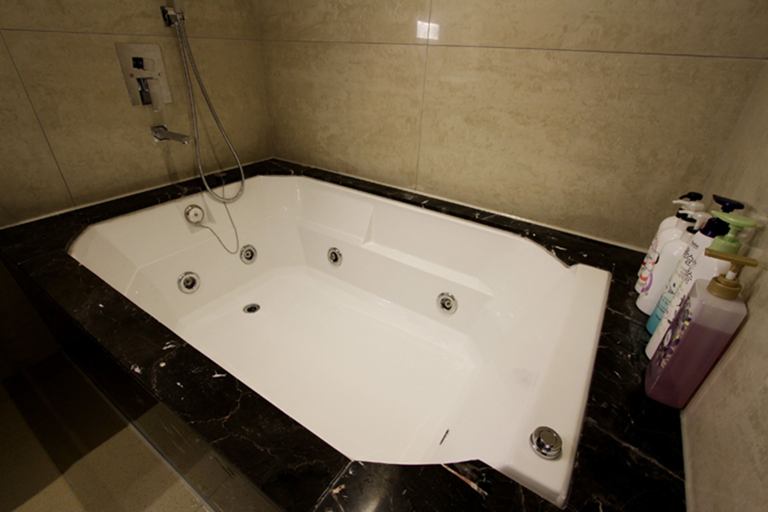 A large, rectangular bathtub with a single faucet and a handheld showerhead, set against a tiled wall.