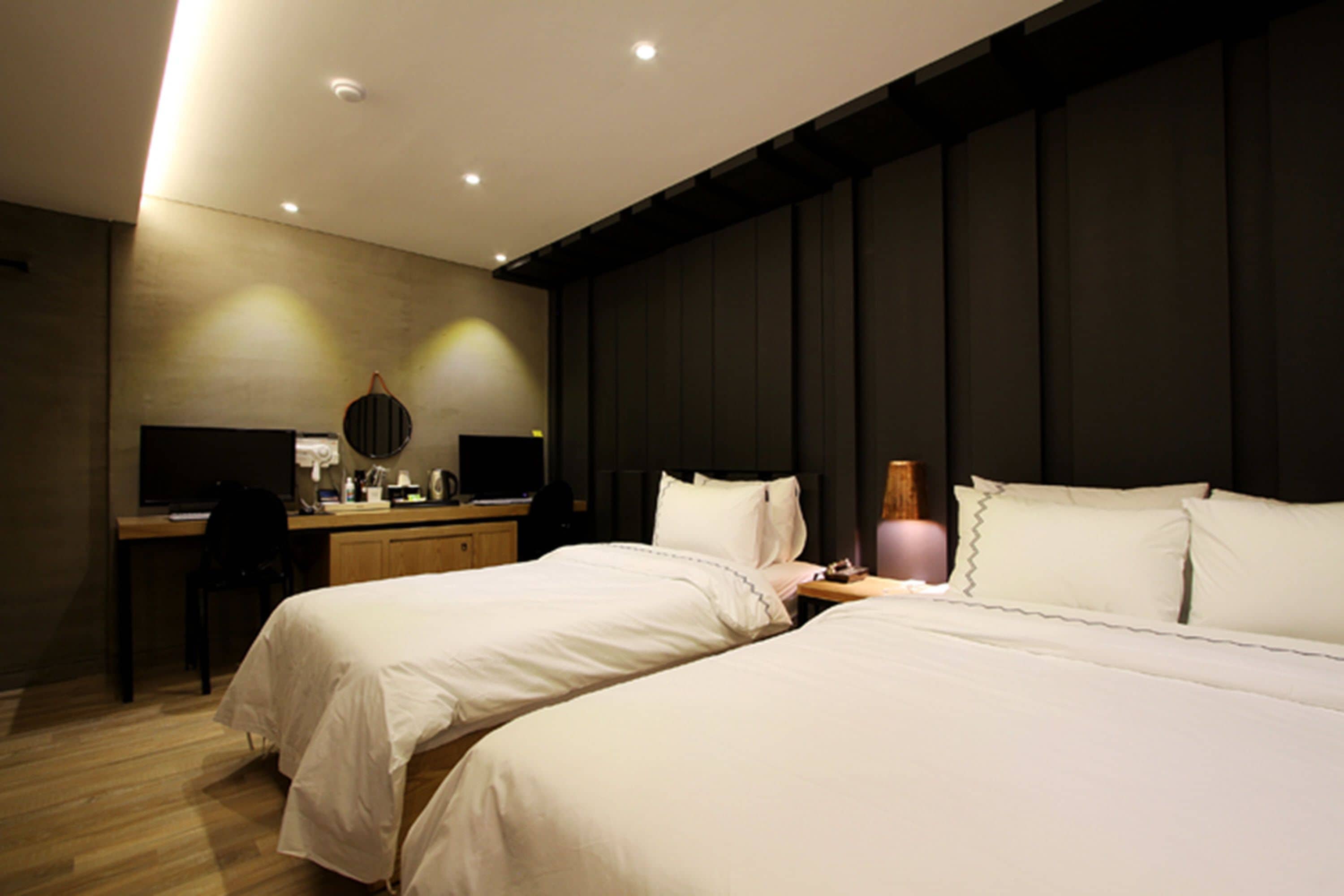Habitación de hotel con dos camas, un escritorio, una silla y un espejo grande.