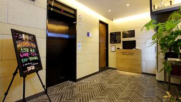 A hotel lobby with a reception desk, a service information board, and an elevator.