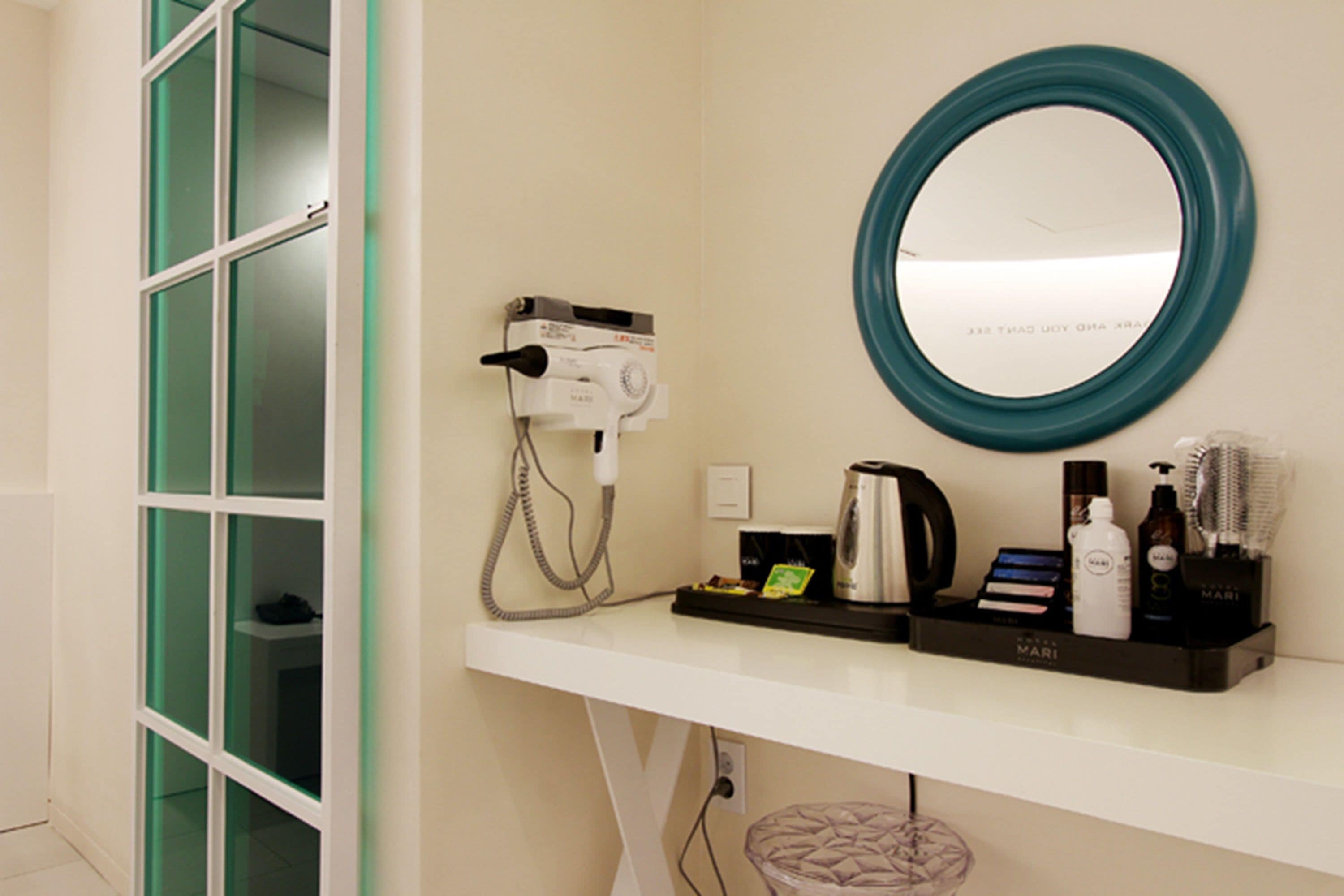 A bathroom with a white vanity, a round mirror, a hairdryer, and toiletries.