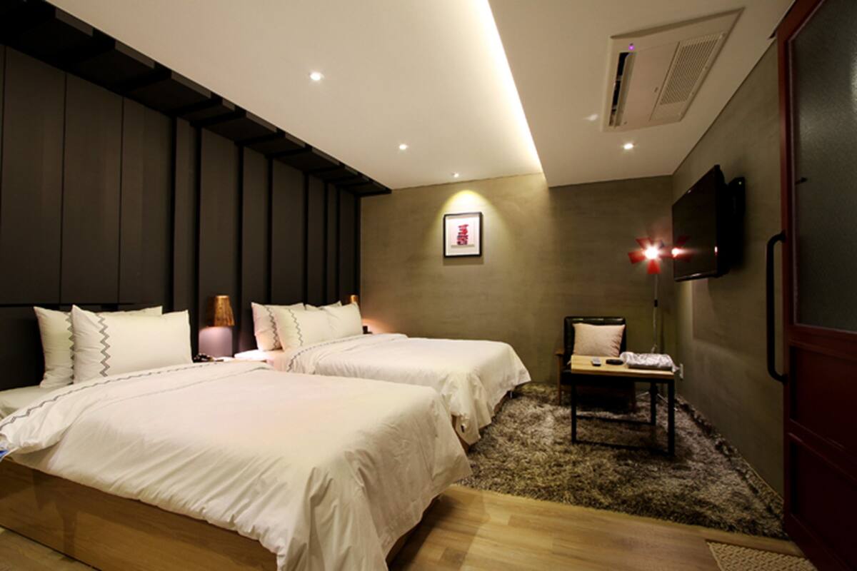 A hotel room with two beds, a flat-screen TV mounted on the wall, and a small table with a chair.