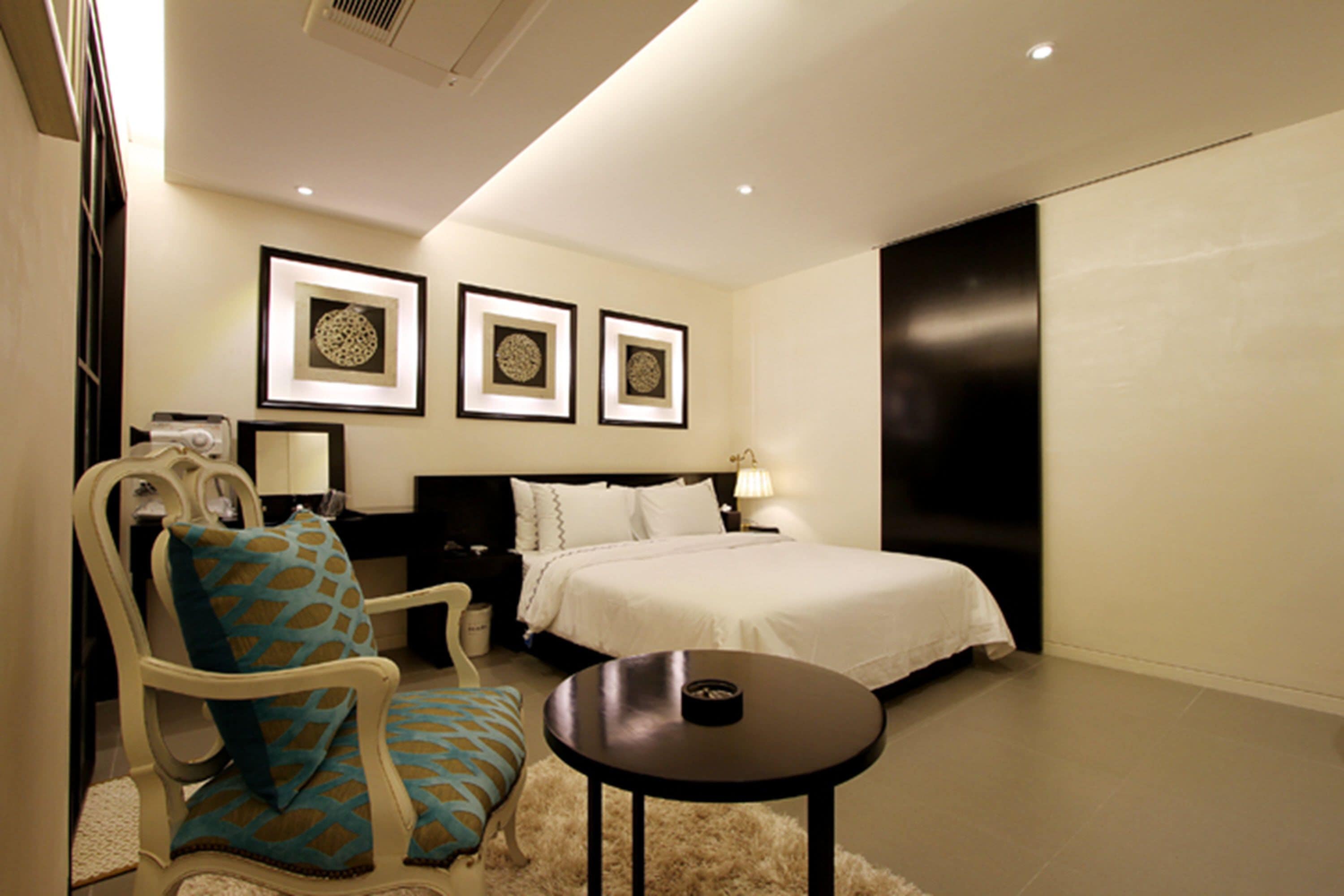 Una habitación de hotel con cama, una silla, una mesita y tres cuadros en la pared.