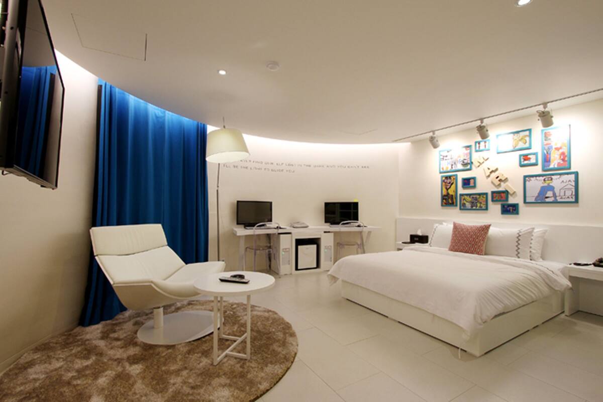 A modern hotel room with a bed, a desk with a computer, a chair, and a TV.