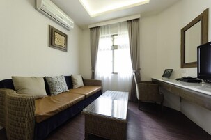 A living room with a sofa, a small table, a chair, a TV, and a window with curtains.