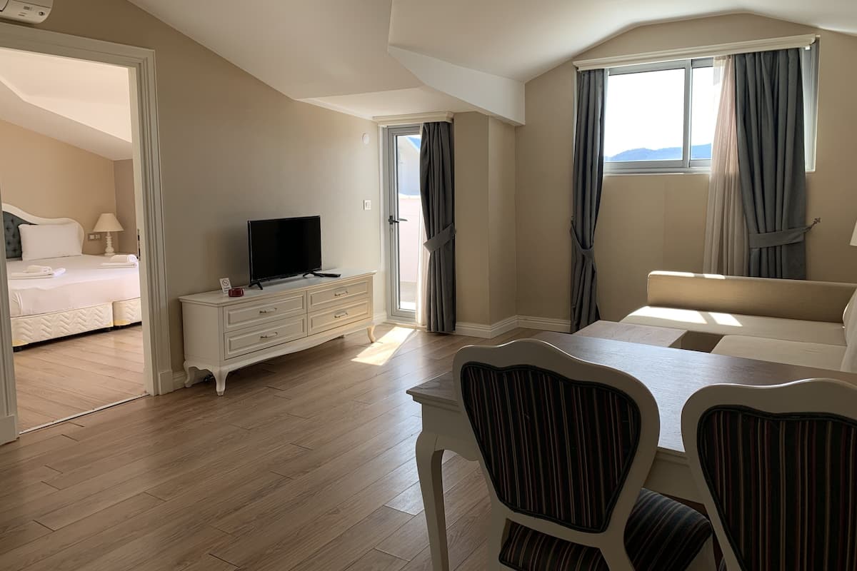 Une chambre d’hôtel moderne, équipée d’un lit, d’un téléviseur posé sur une commode, d’une table à manger avec des chaises et de grandes fenêtres avec des rideaux.