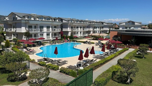 Een hotel met een zwembad, ligbedden en rode parasols.