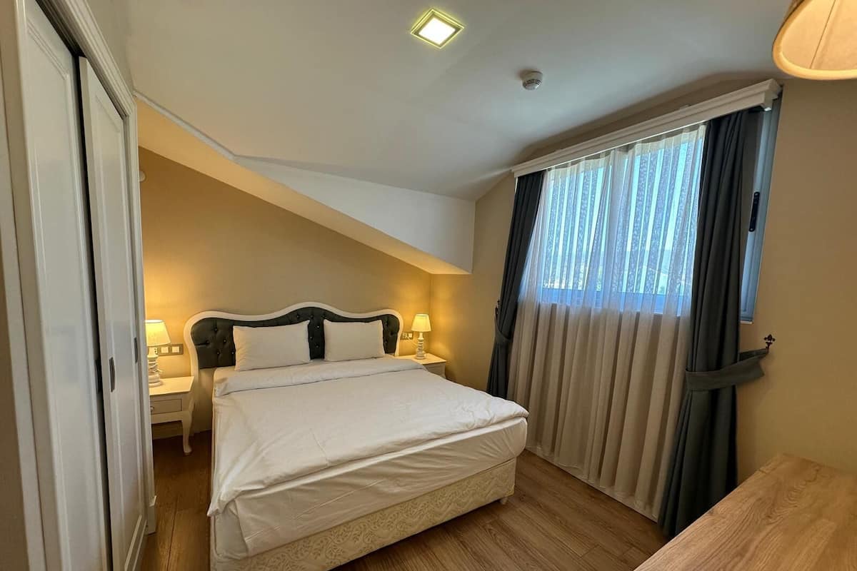 Une chambre d’hôtel comprenant un lit, des tables de chevet, un bureau, une fenêtre avec des rideaux et un luminaire au plafond.