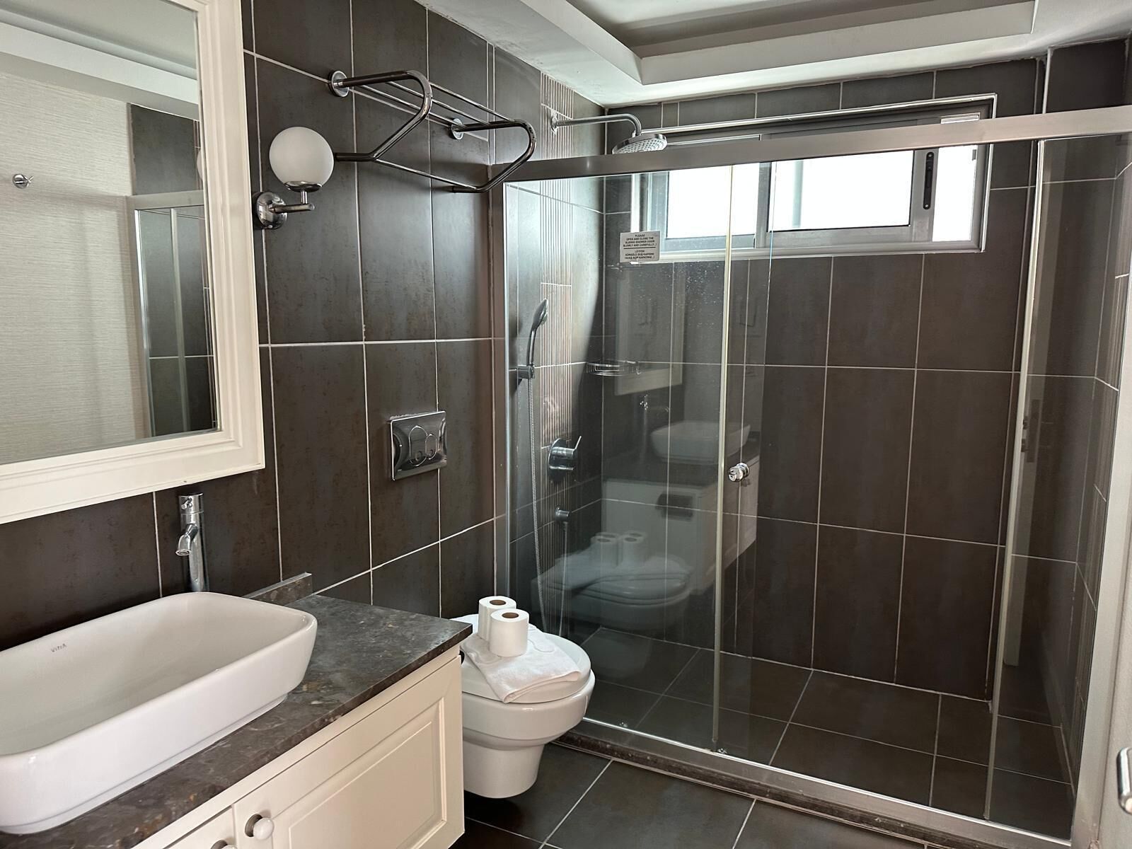 A modern bathroom with a large mirror, a white sink, a toilet, and a glass-enclosed shower area.