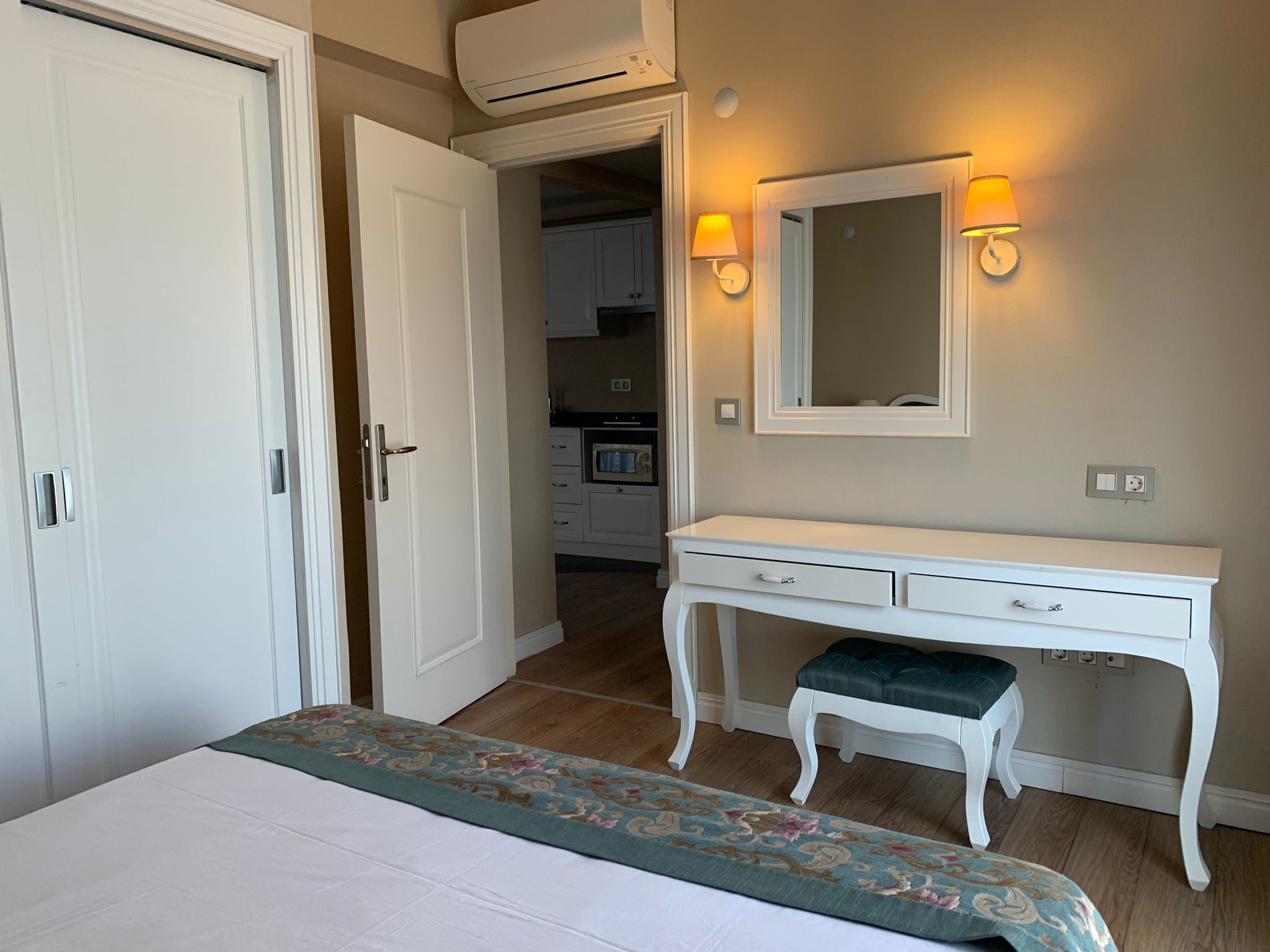 A bedroom with a bed, a white dresser, a mirror, and a small stool.