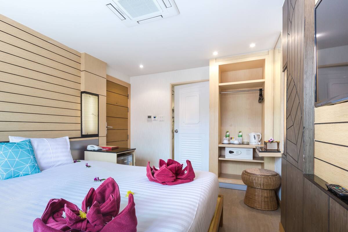 A hotel room with a large bed, a bedside table, a wardrobe, a bathroom, and a small seating area.