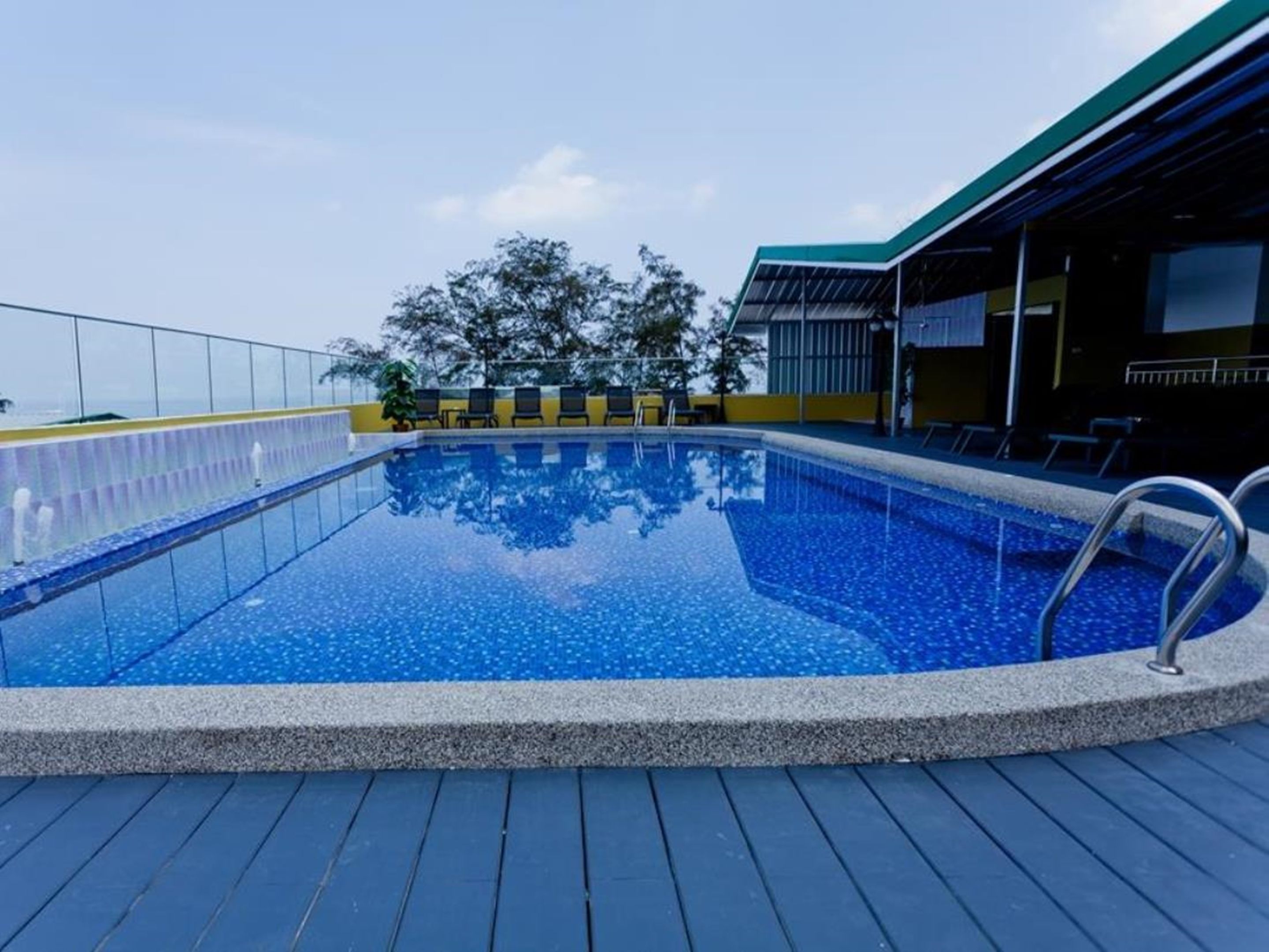 A swimming pool with a clear blue water surface, surrounded by a wooden deck and a glass balustrade.