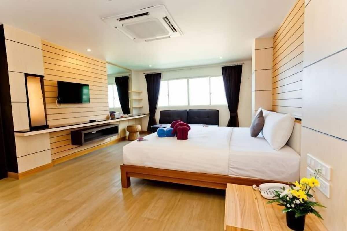 A modern hotel room with a bed, bedside table, TV, and a window with curtains.