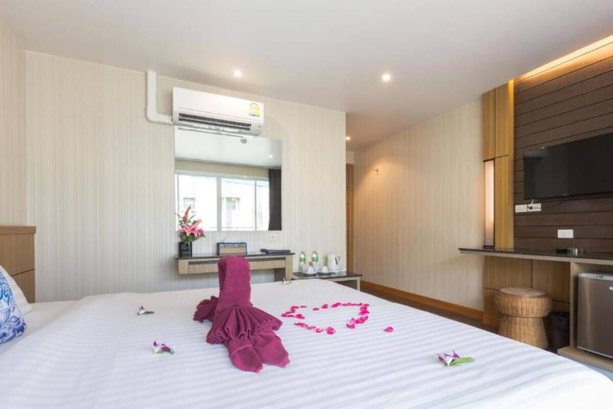 A hotel room with a bed, a TV mounted on the wall, a small fridge, and a wooden cabinet.