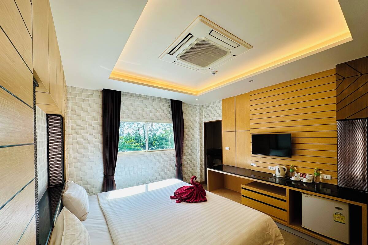 A modern hotel room with a large bed, a flat-screen TV, a small kitchenette, and a window with curtains.