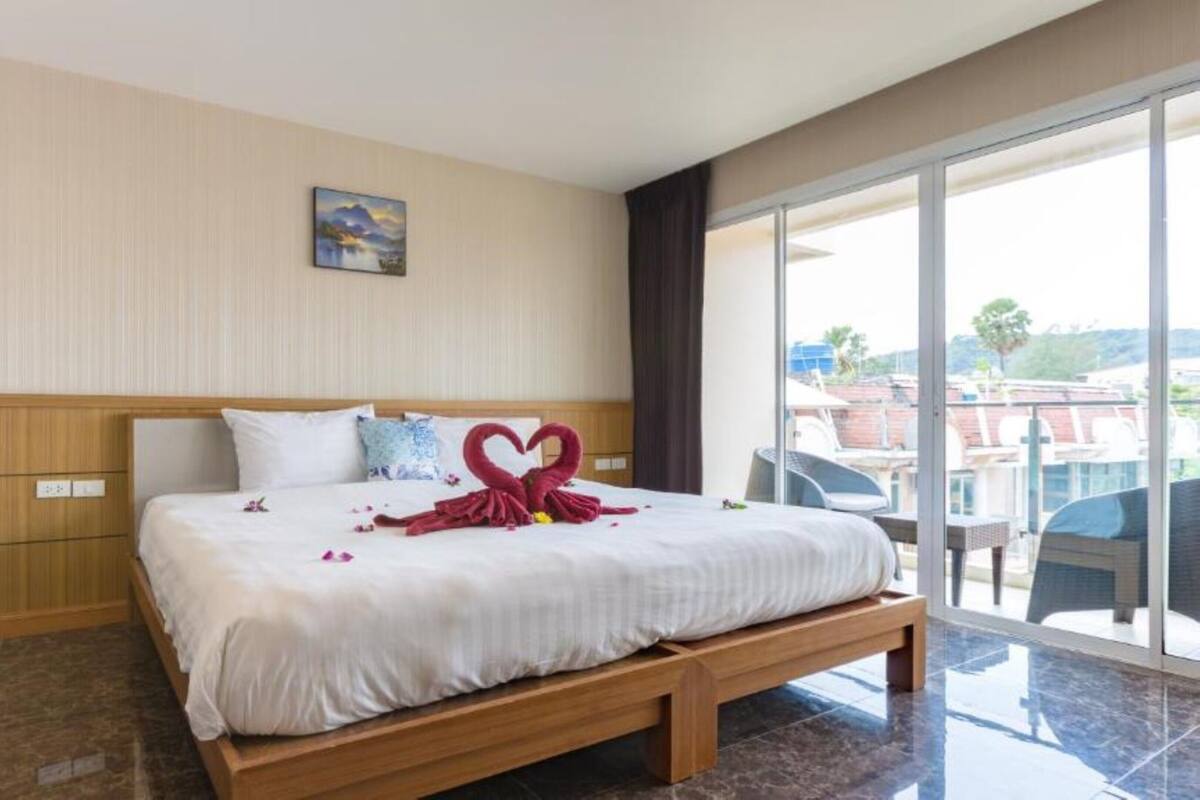 A hotel room with a bed, a wooden headboard, a painting on the wall, and a balcony with a view.