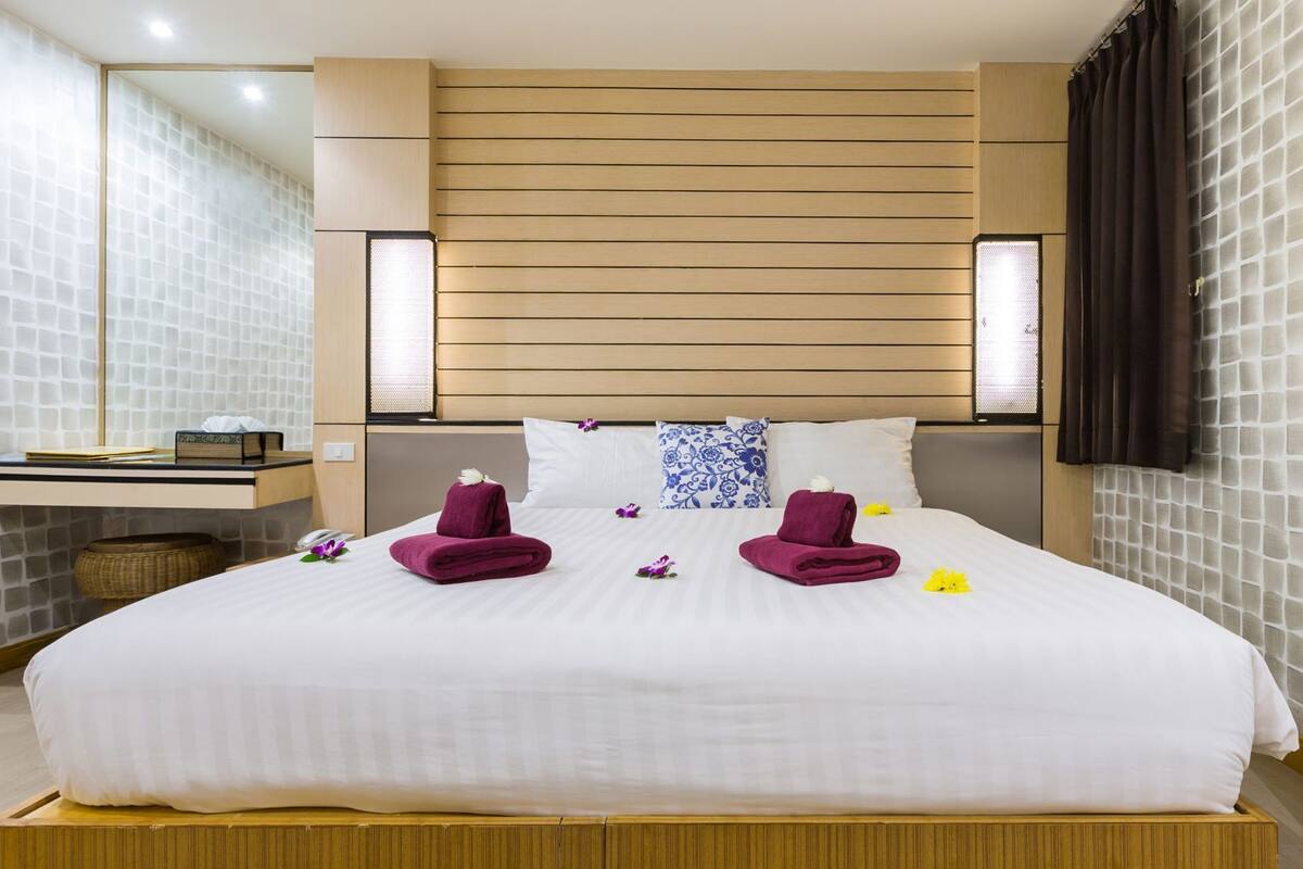 A hotel room with a large bed, wooden headboard, two bedside tables, a mirror, and a wall-mounted TV.