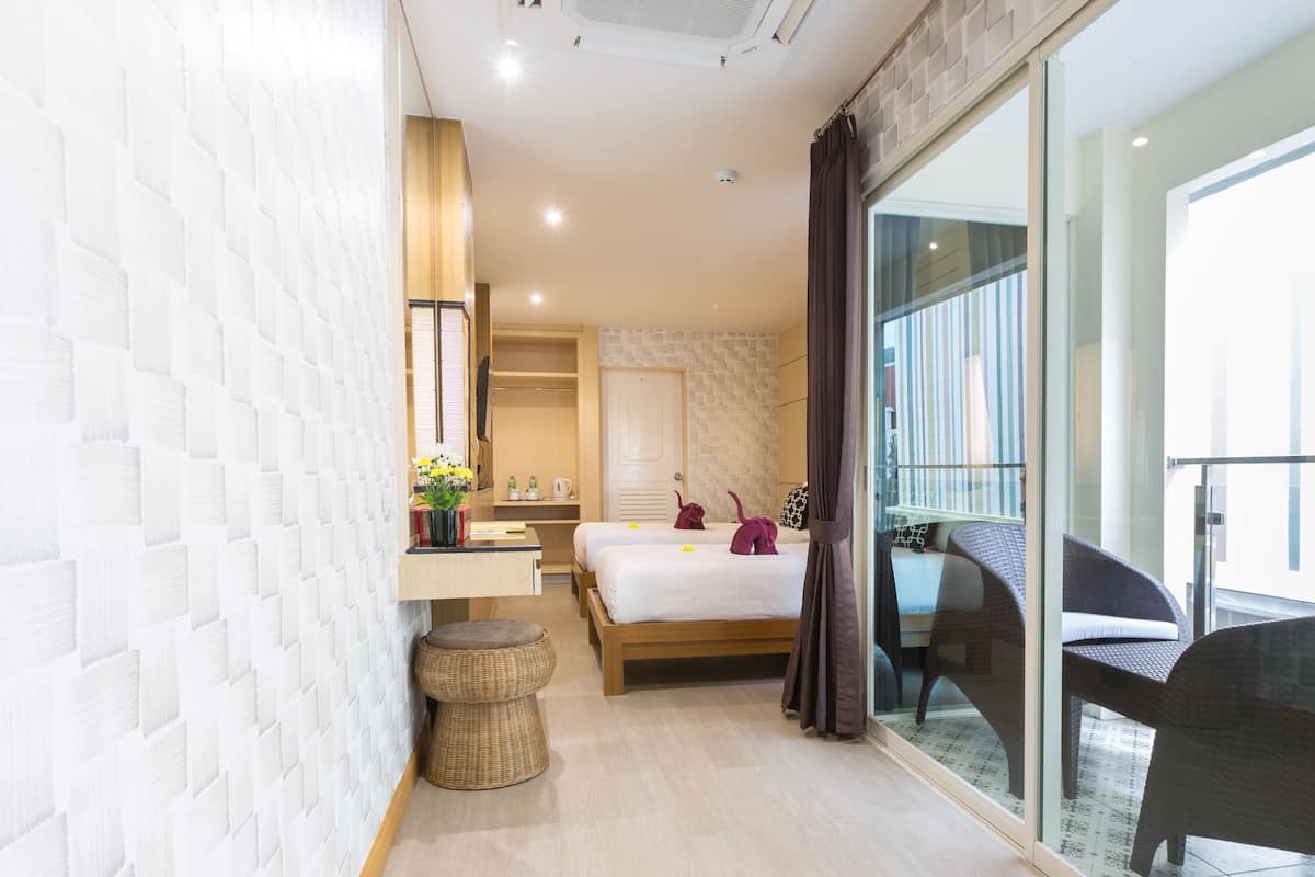 A modern hotel room with a large bed, a small desk, a wicker stool, and a balcony with a chair.