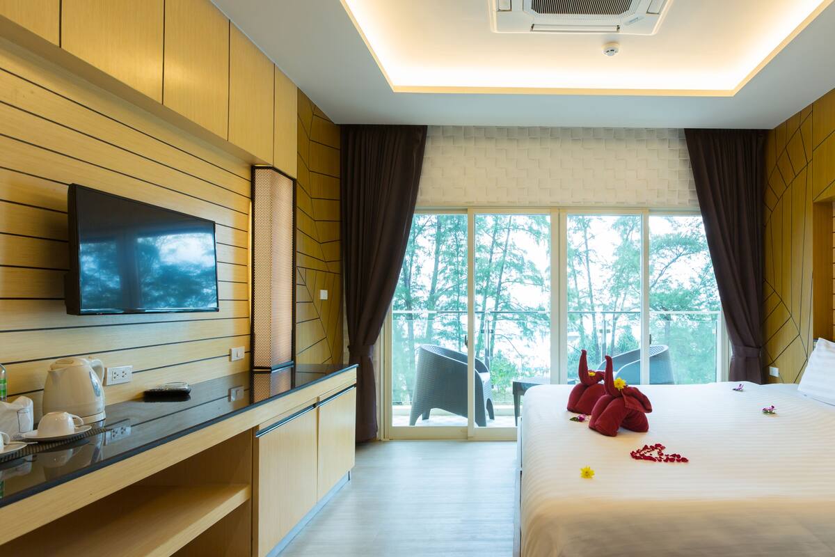 A modern hotel room with a large bed, a flat-screen TV, a desk with a coffee maker, and a view of the outdoors.