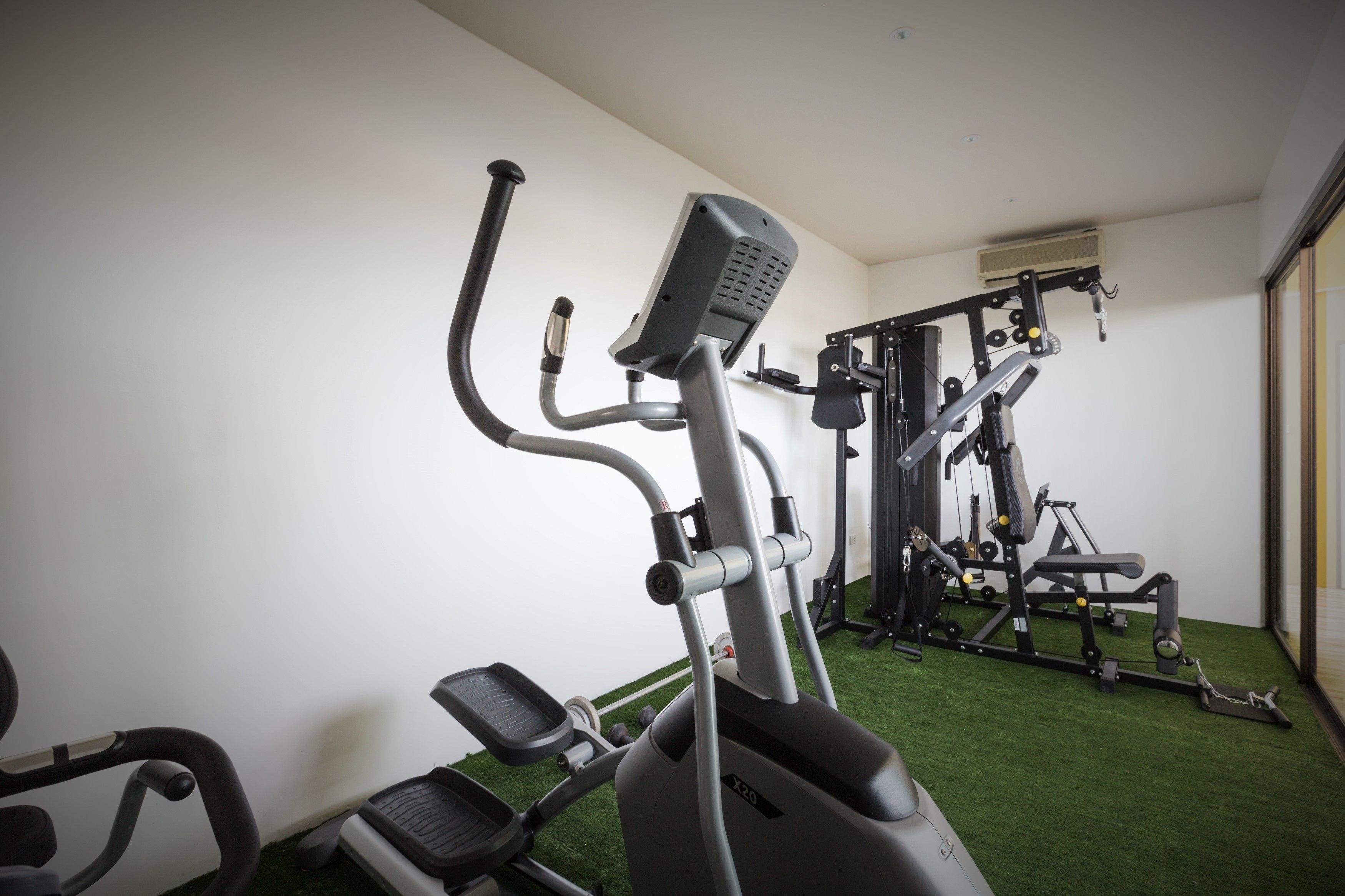 A gym with exercise equipment, including an elliptical trainer and weight machines, on a green floor.