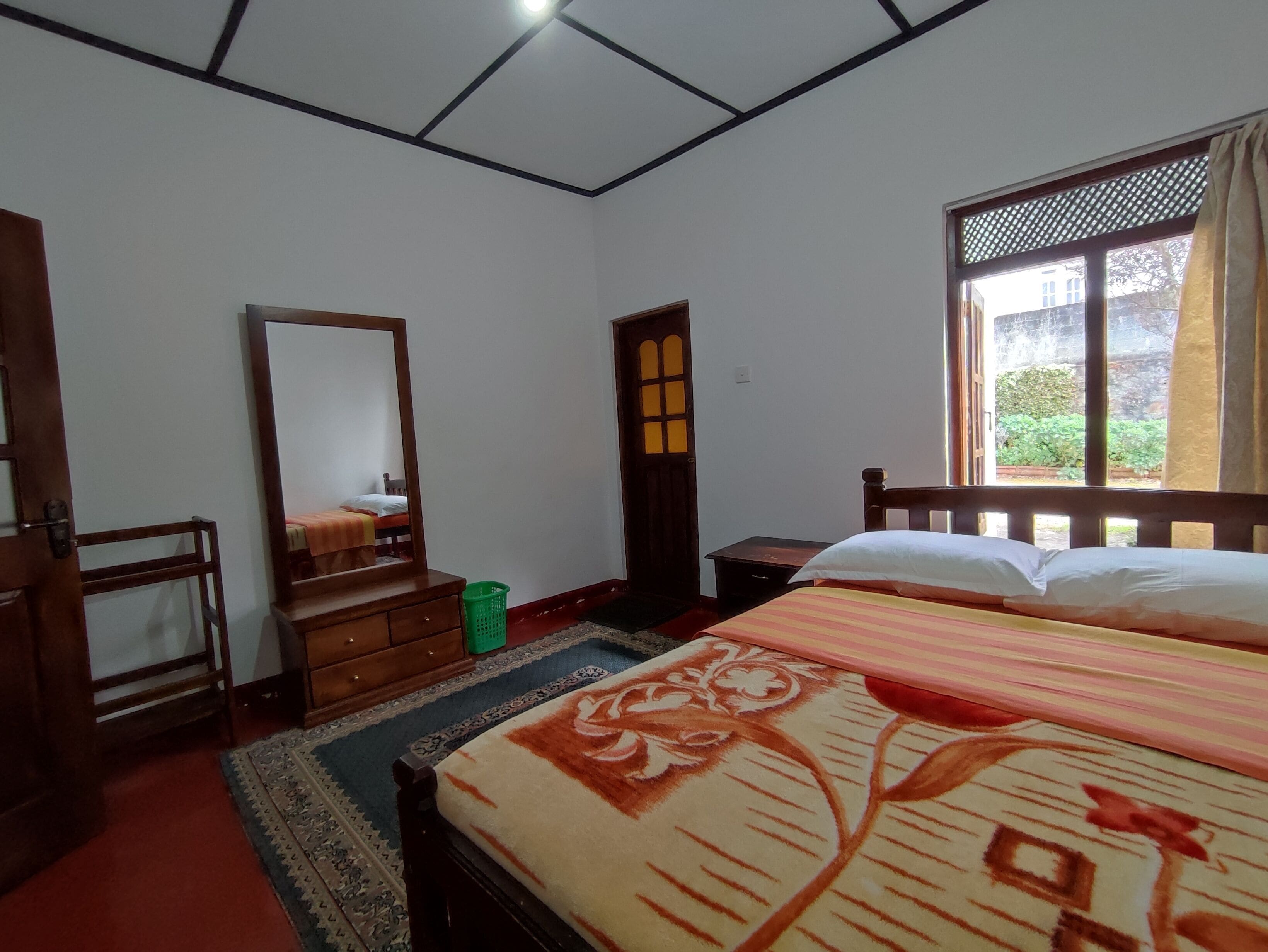 Une chambre à coucher avec un lit, une commode, un miroir, une fenêtre et une porte.