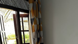 Una cama con ropa blanca, una ventana que ofrece vistas a la vegetación y una cortina estampada.