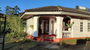 Una casa de un piso con techo de tejas, un porche con barandilla y un pequeño jardín.