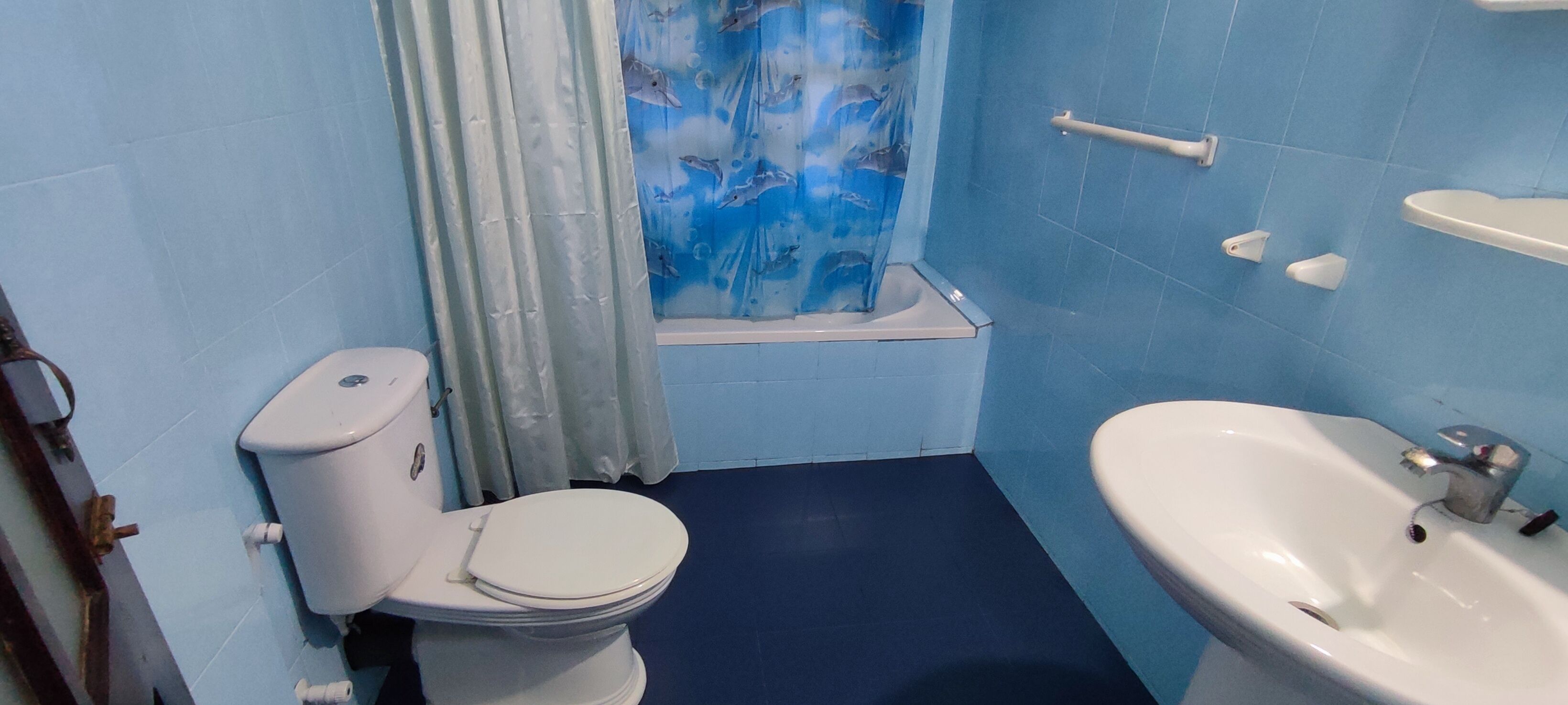 A bathroom with a toilet, shower curtain, sink, and blue tiled walls.