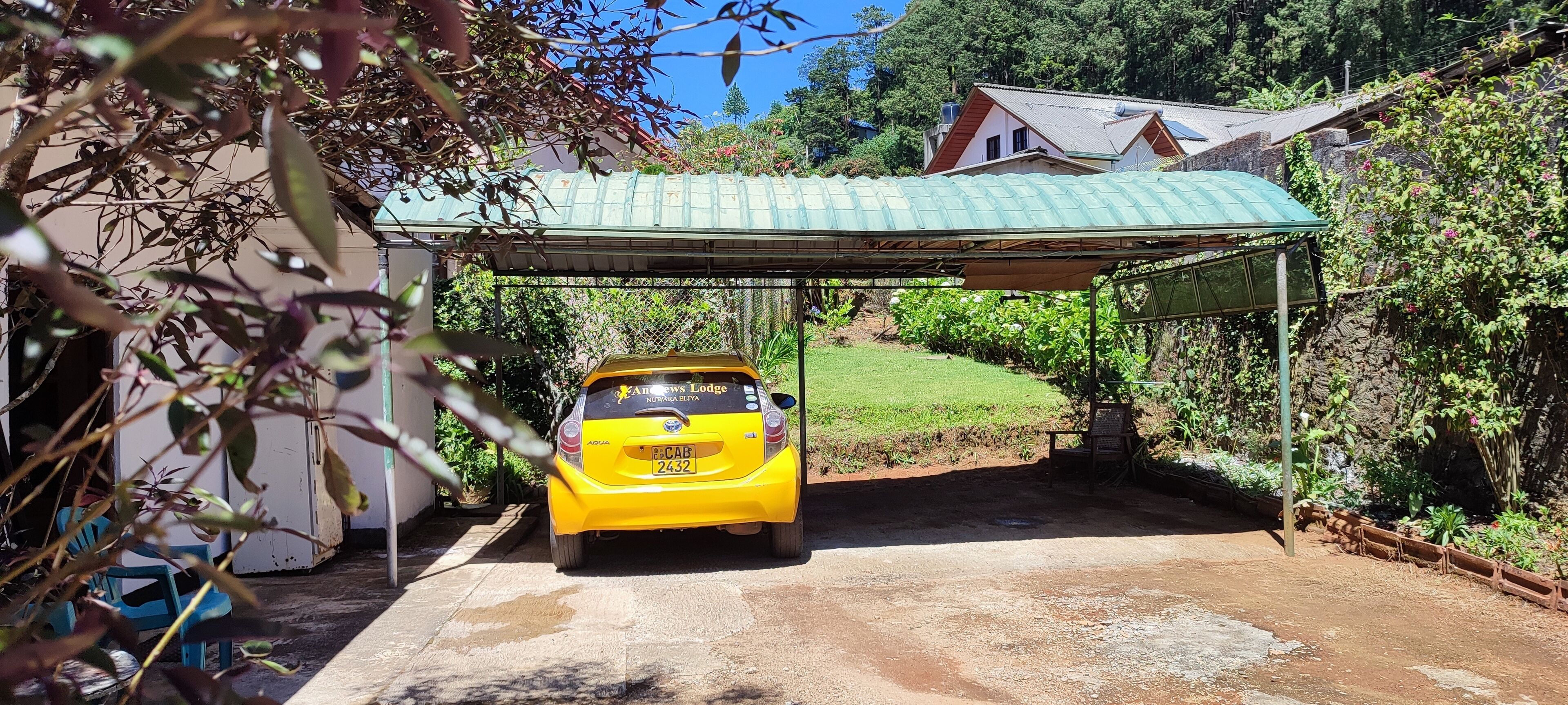 Um carro amarelo estacionado sob uma cobertura, com uma casa ao fundo.