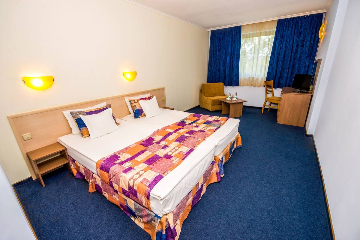 A hotel room with a large bed, two bedside lamps, a desk with a chair, and a TV.