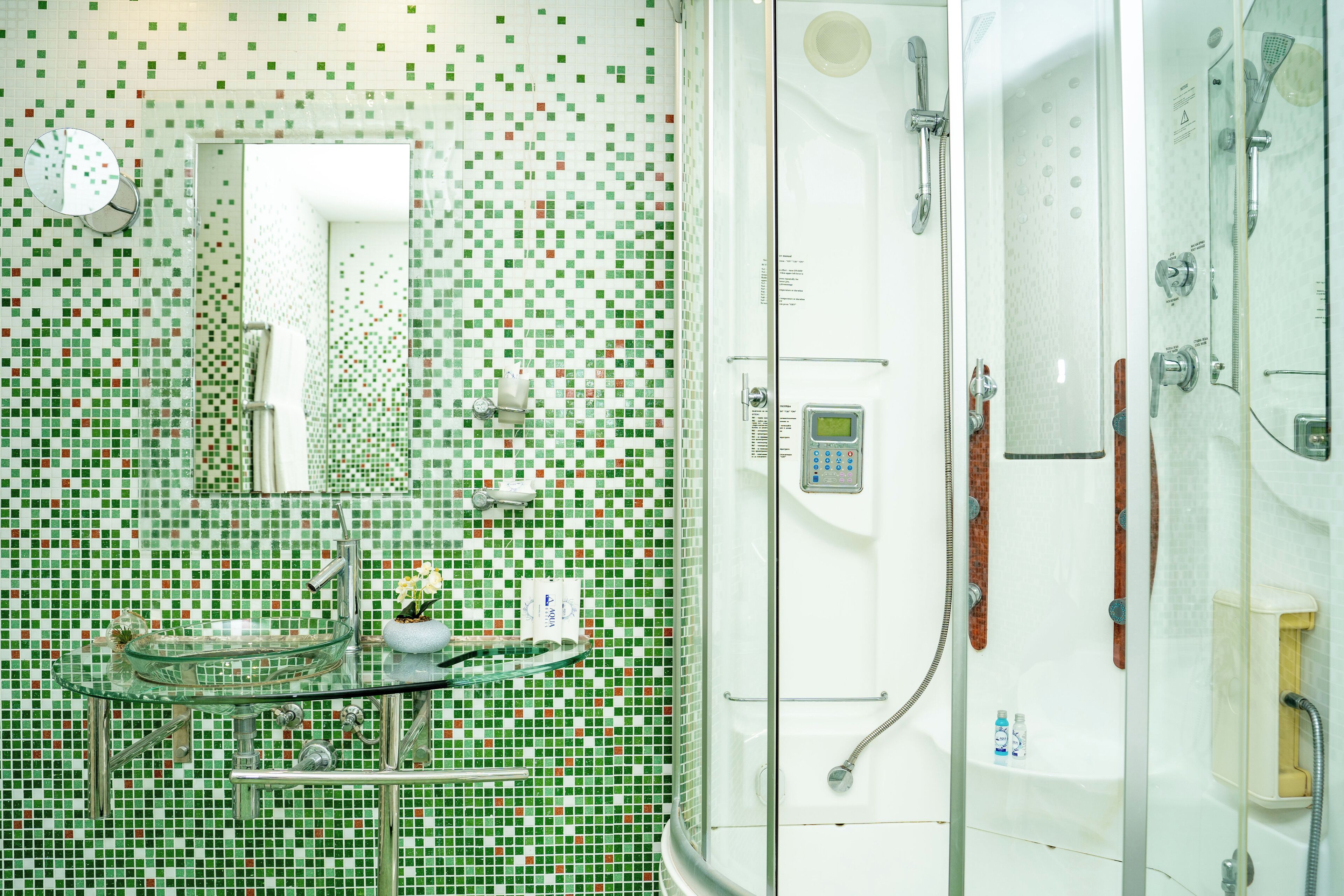 A bathroom with a mosaic tile wall, a glass sink, and a shower enclosure.