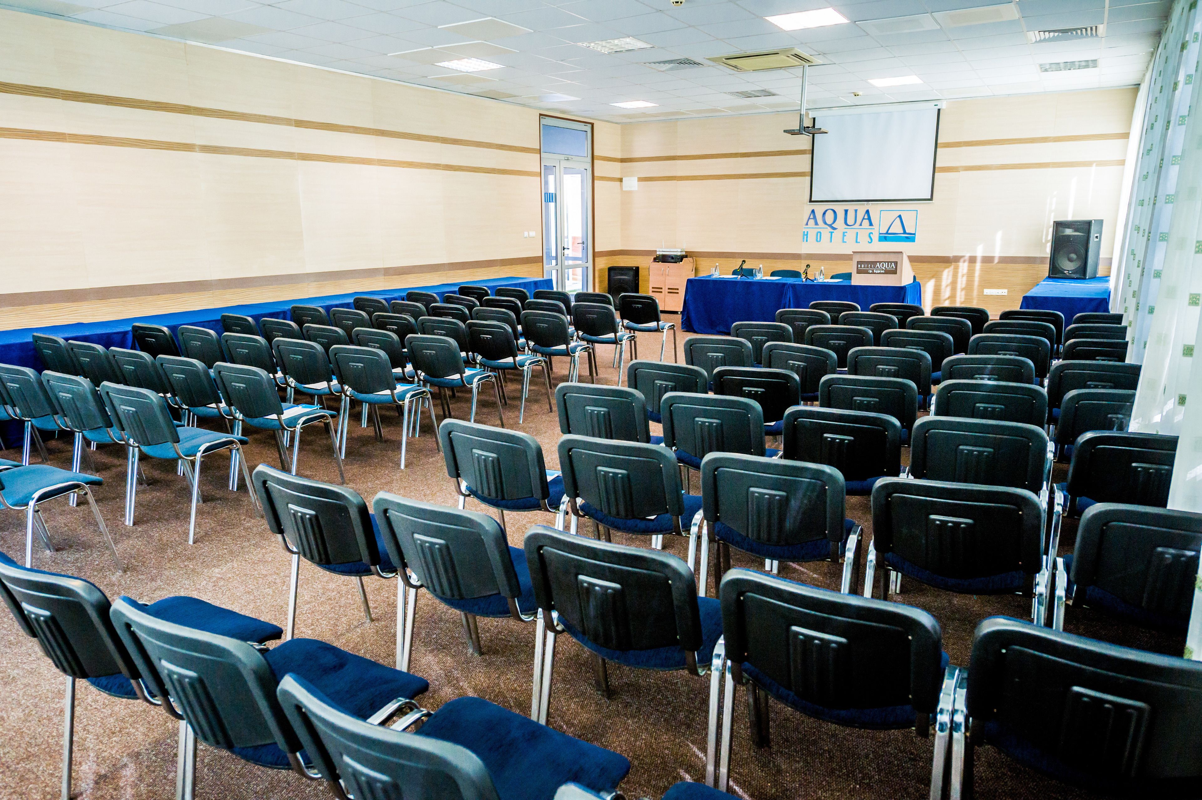 Un salón de conferencias con filas de sillas, un atril y una pantalla.