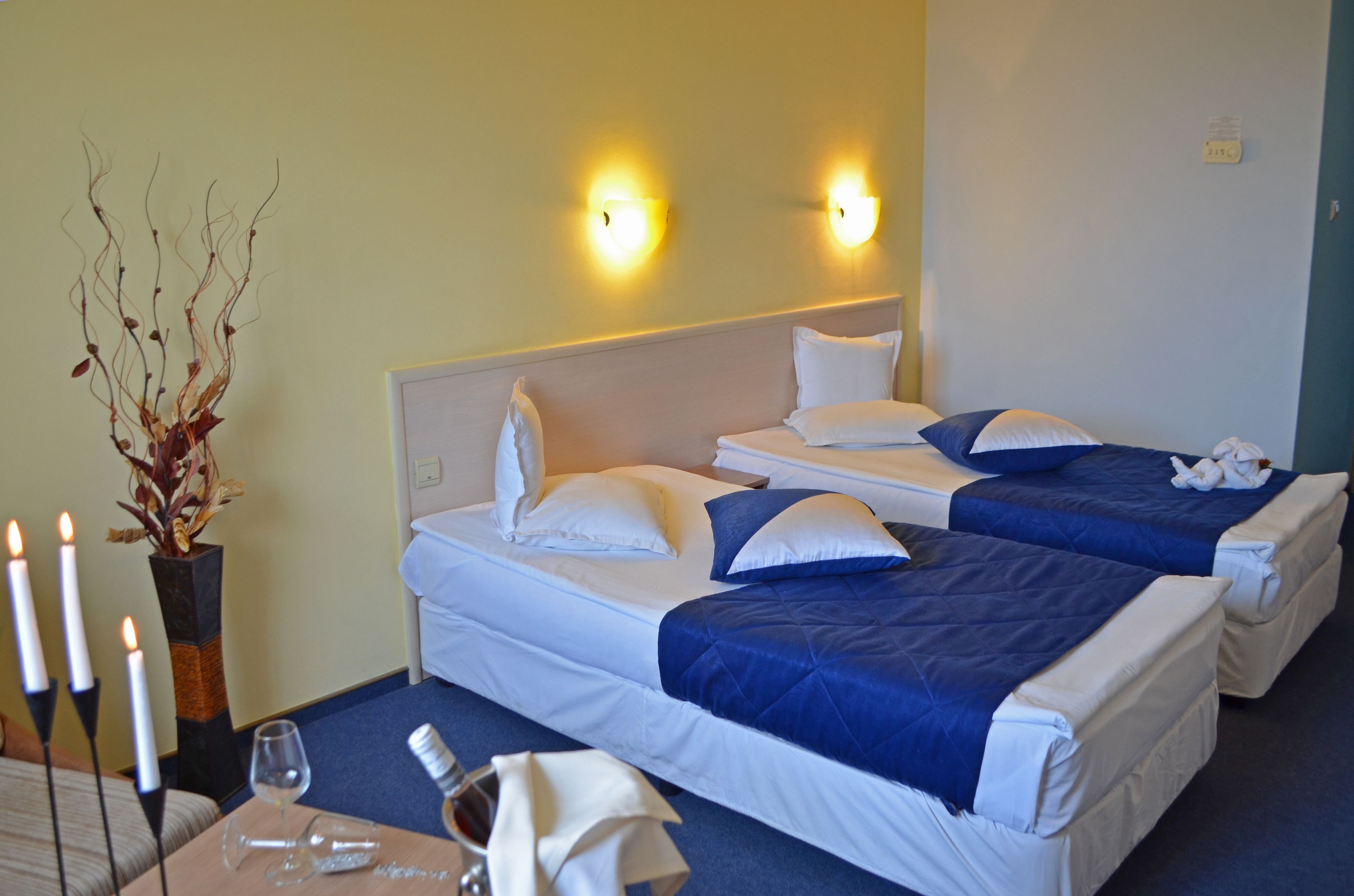 Habitación de hotel con dos camas, un florero con ramas, velas y una mesa con un vaso y servilleta.