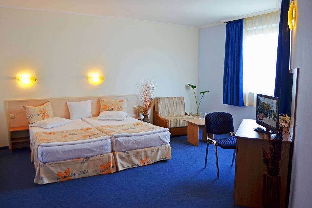 A hotel room with a double bed, a desk with a chair, a TV, and two wall-mounted lights.
