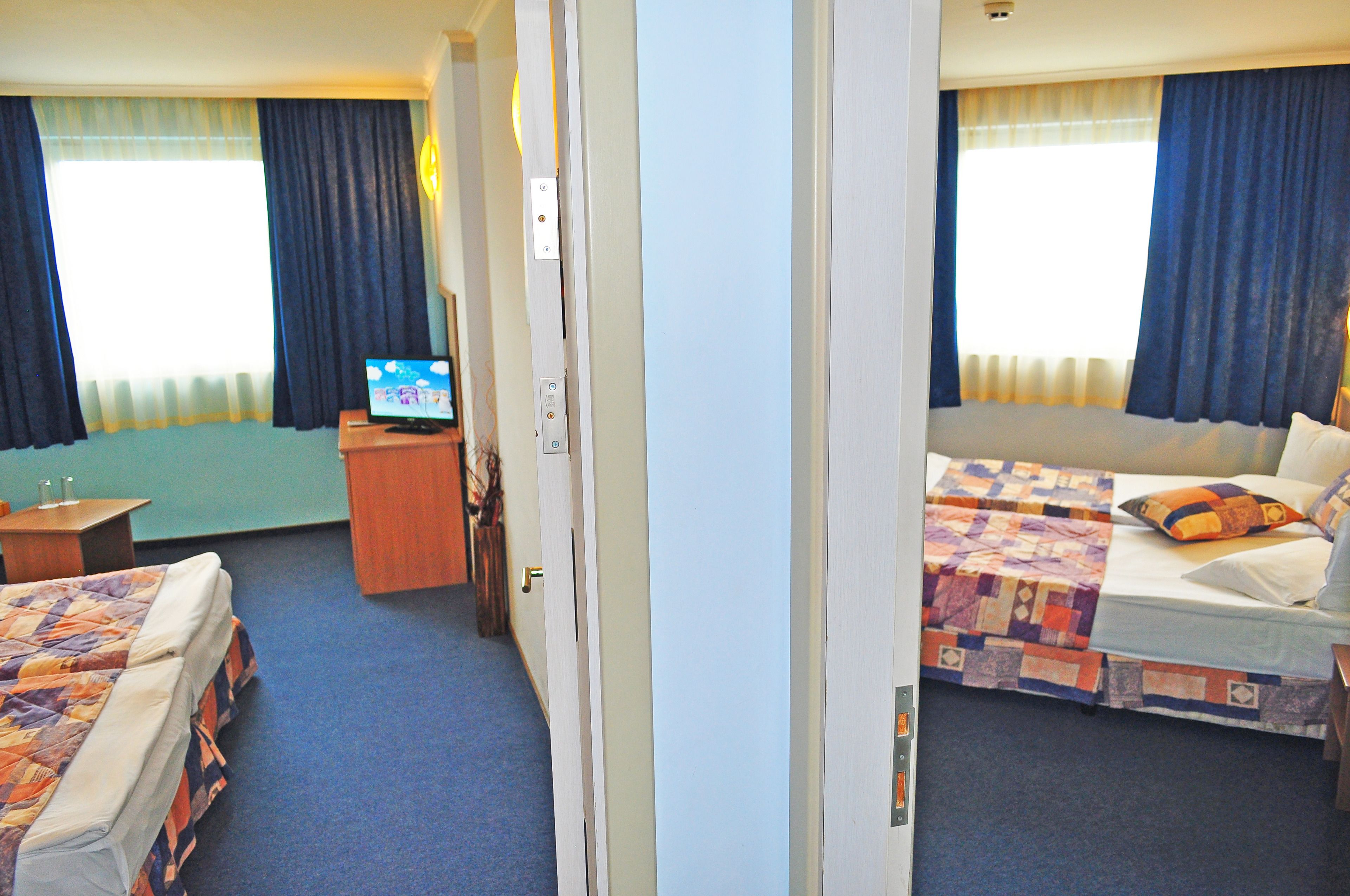 A hotel room with two beds, a desk, a television, and a window with curtains.