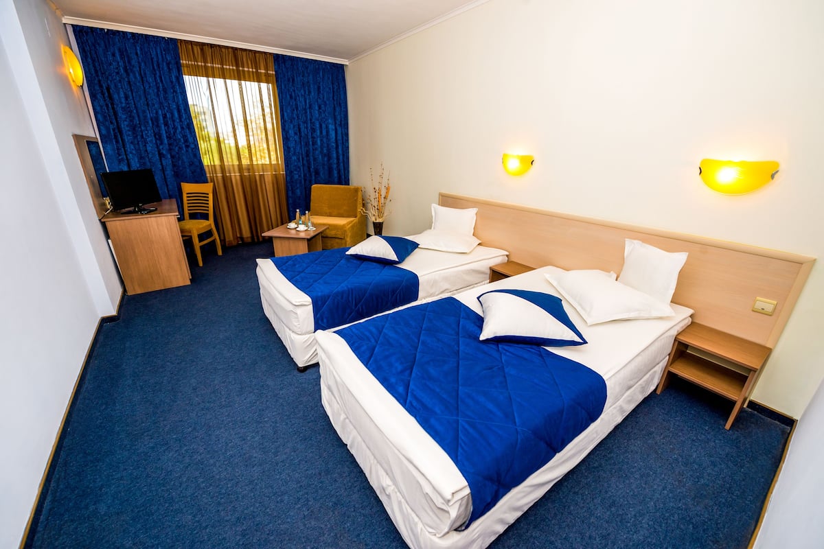 A hotel room with two beds, a desk with a computer, a chair, and a small table with a vase.