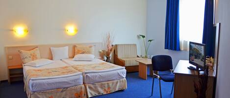 Habitación de hotel con cama doble, escritorio con silla, televisor y ventana con cortinas.