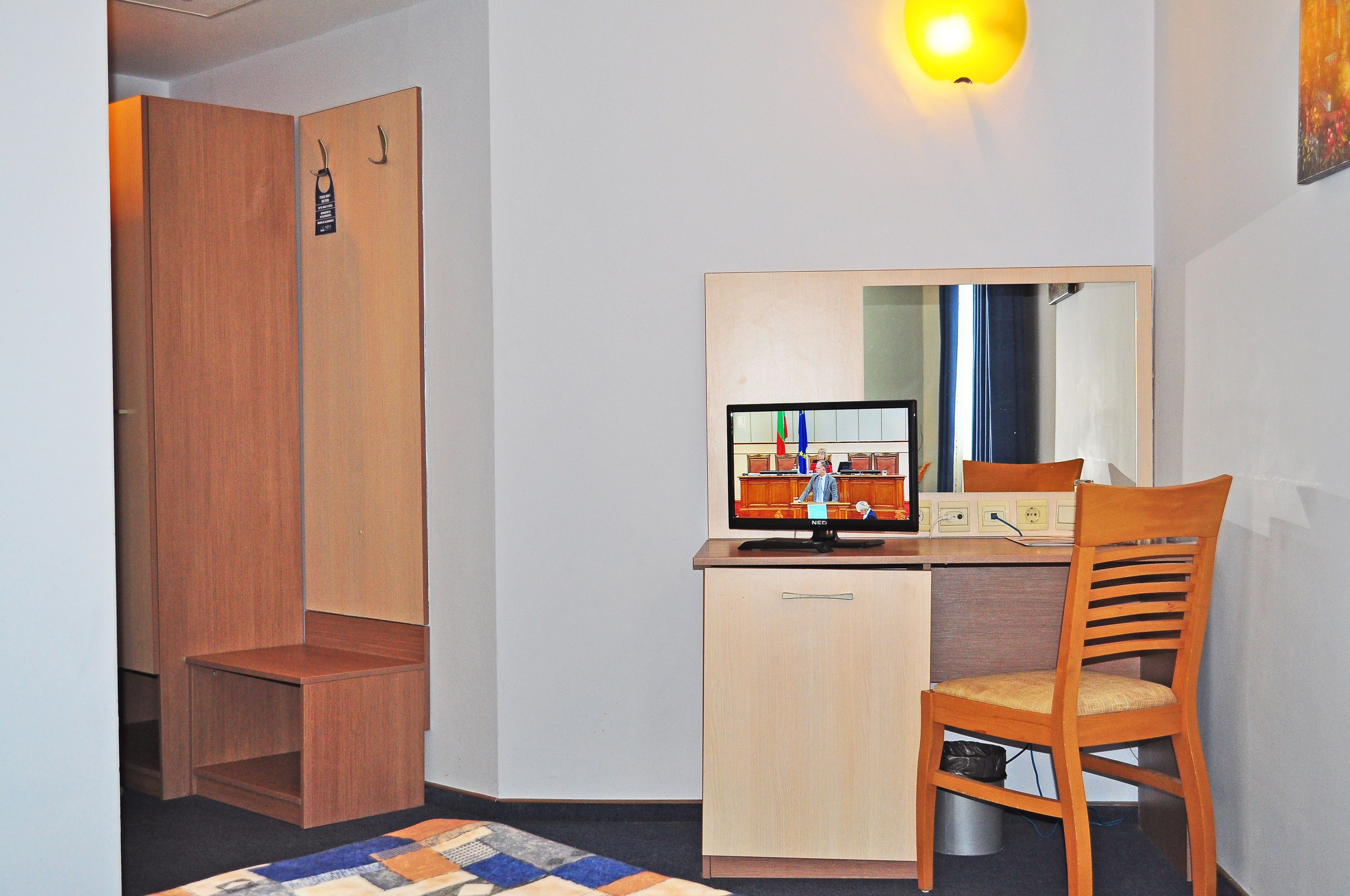 A small room with a wooden wardrobe, a desk with a computer monitor, and a chair.