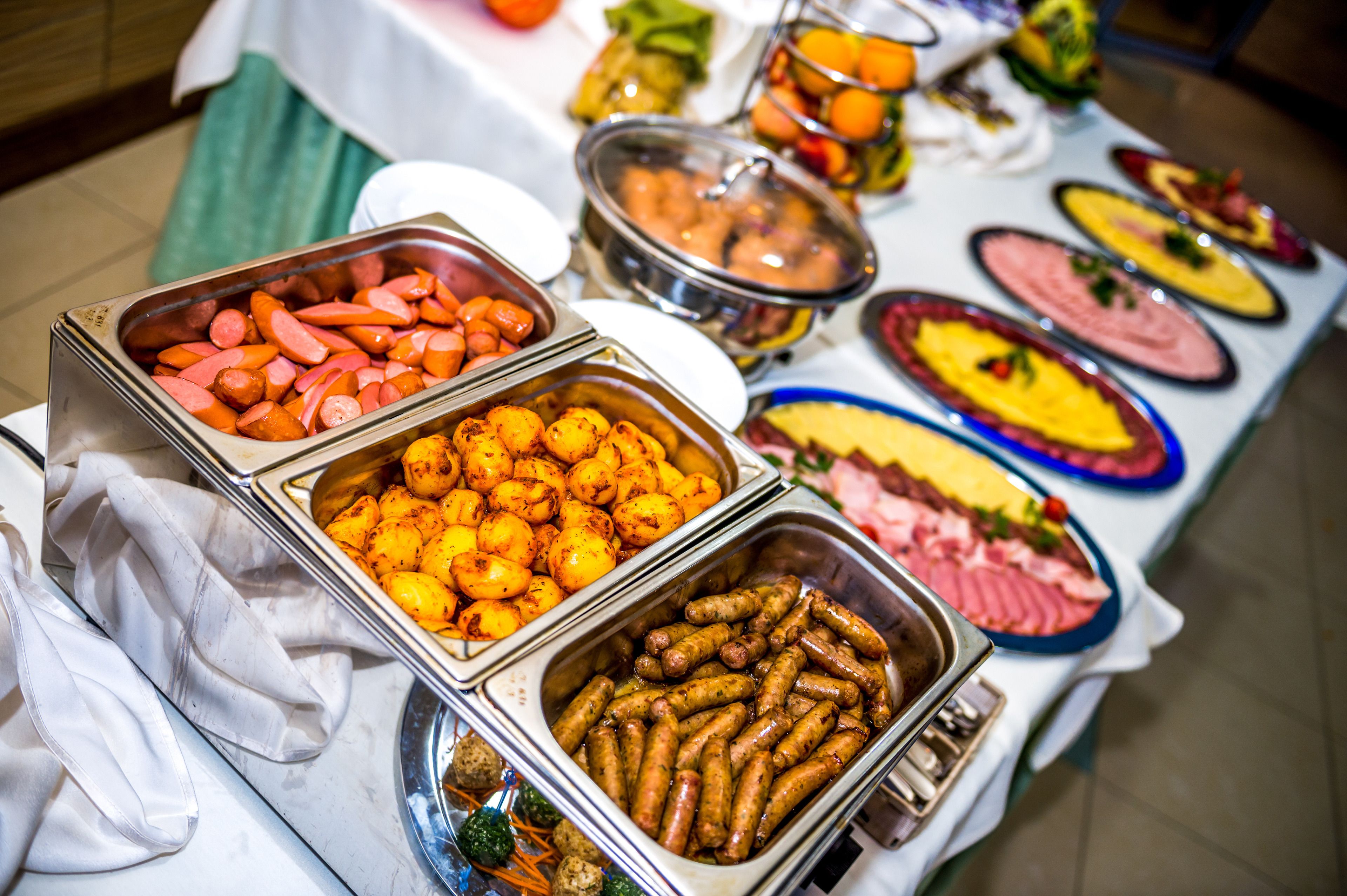 A buffet table with various food items including sausages, carrots, and potatoes.